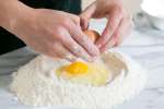 cracking an egg into a flour well to make pasta Shot