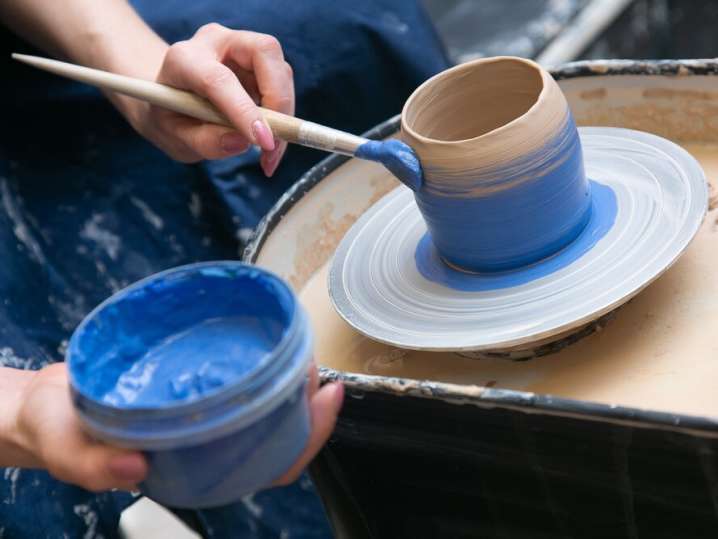 a woman painting a pottery vase with blue paint Shot