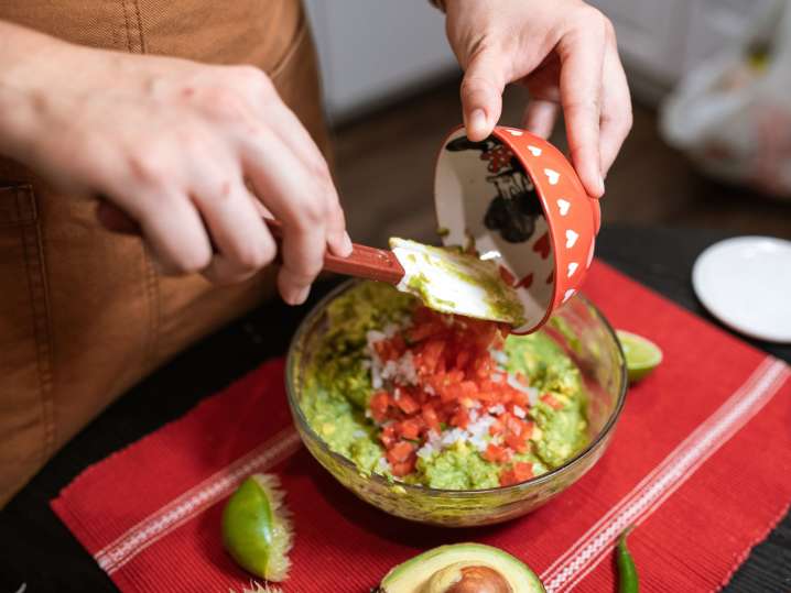 Boston - Person preparing guacamole in a molcajete with diced tomatoes on top Shot