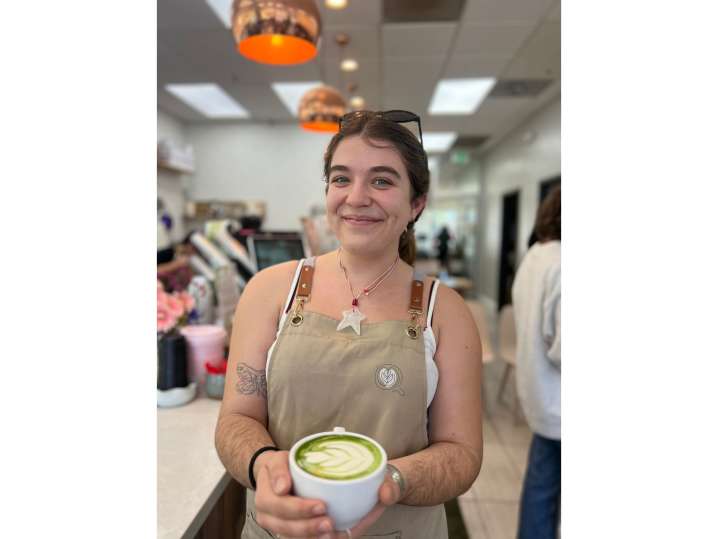 Bay Area - Student in an apron proudly displaying her finished matcha latte with heart-shaped foam art Shot