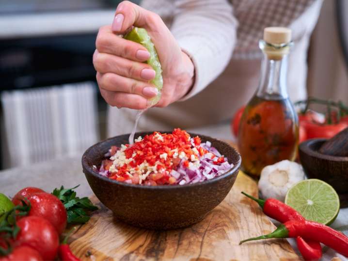Boston - Hand squeezing lime over a bowl of freshly made salsa with chopped tomatoes, onions, and herbs Shot