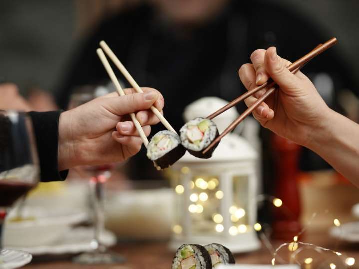 Boston - Two people clinking sushi rolls over a meal, celebrating their creations Shot