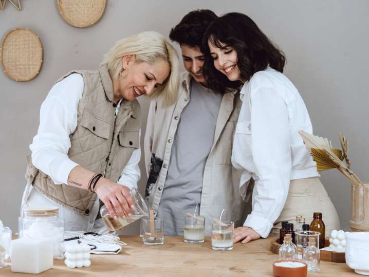 Boston - Two women assisting a third person in pouring wax during a cozy group candle-making session Shot