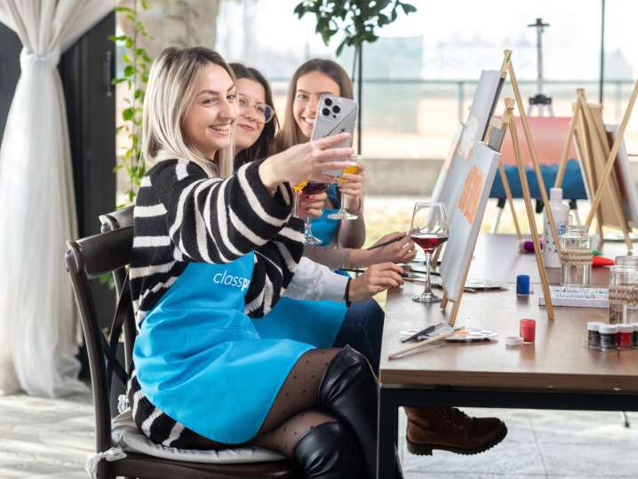 Boston - Three women smiling and enjoying drinks while painting at a paint and sip party near a window Shot