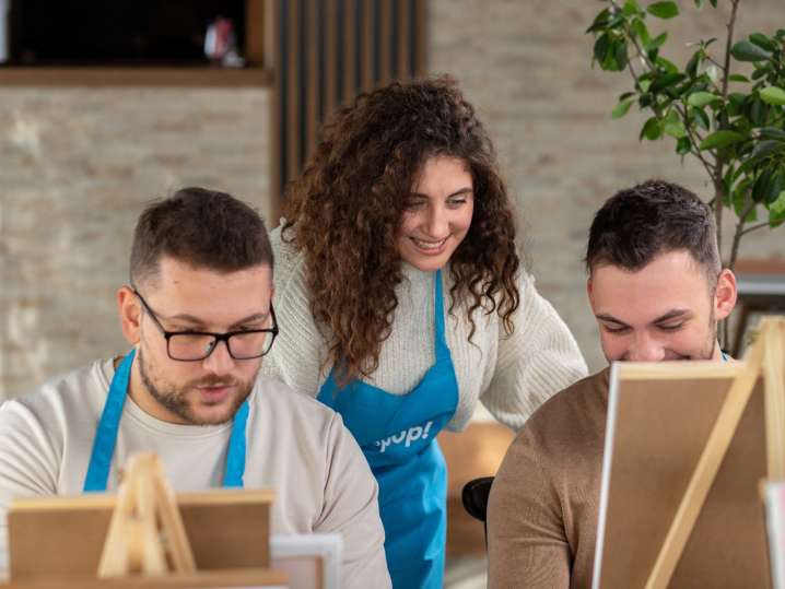 Boston - Instructor guiding two men as they paint at their easels in a cozy indoor setting Shot