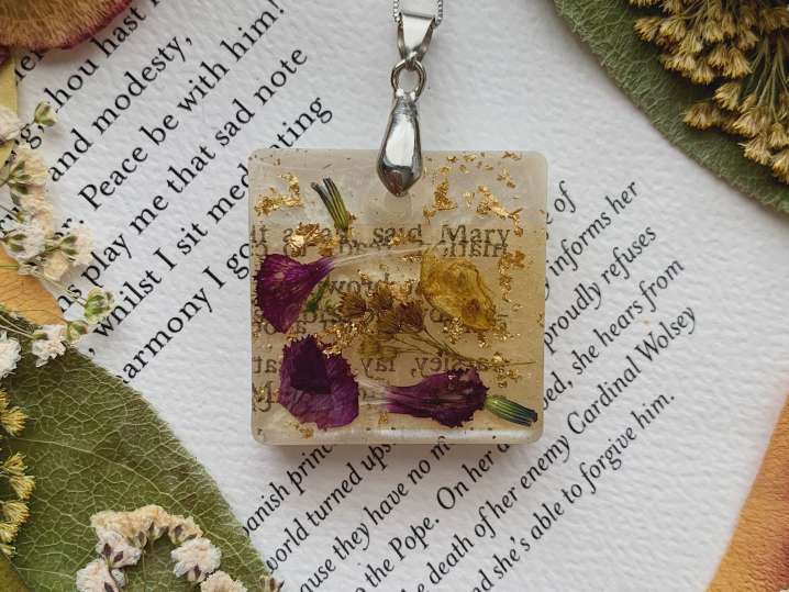 Bay Area - Square resin pendant with dried flowers and small purple petals, displayed on an open book page Shot