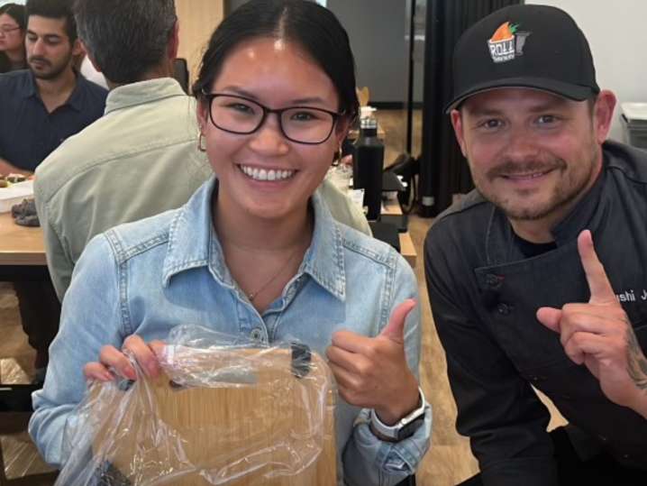 Toronto - Smiling participant posing with a chef while holding her freshly made sushi roll Shot