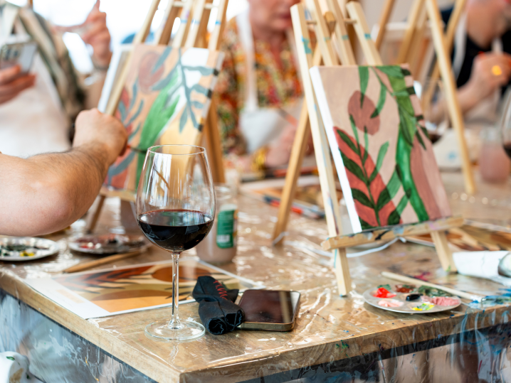 Chicago - Close-up of paint and sip participants painting leafy artwork on easels with wine glasses on the table Shot