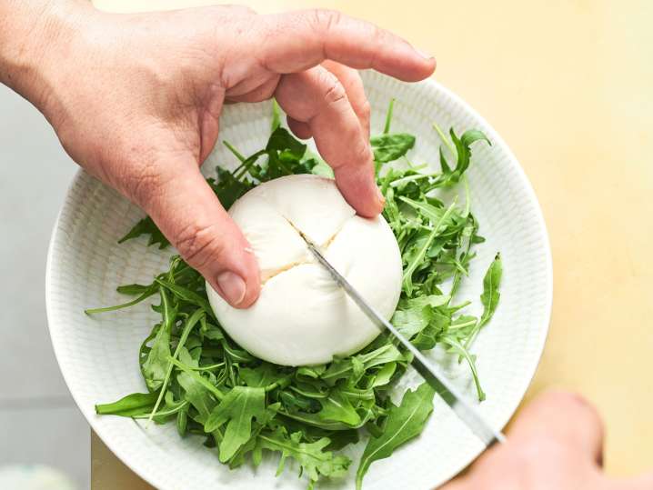 close up of a person's hands cutting buratta chese with a knife over a bend of arugula salad | Classpop Shot
