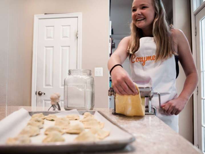 a young girl is laughing while wearing Cozymeal apron and rolling pasta dough | Classpop Shot