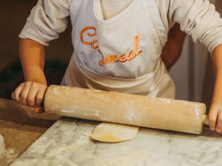 a child with Cozymeal apron on is rolling pasta dough | Classpop Shot