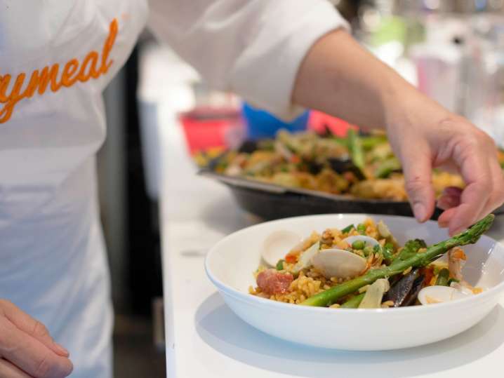 plating seafood and chicken paella with Cozymeal apron on | Classpop Shot