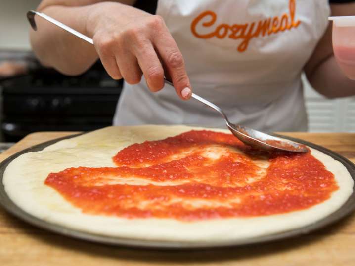 adding tomato sauce on the base of the pizza | Classpop Shot