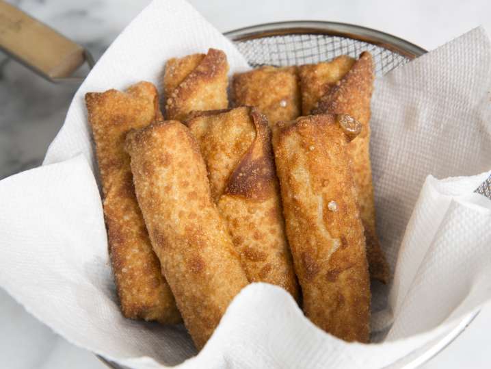fried eggrolls draining in a spider strainer Shot