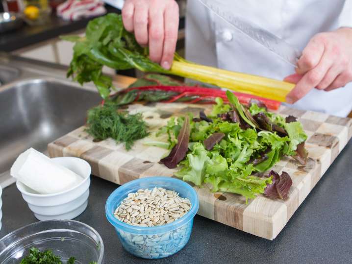 chef chopping vegetables and salad greens on a cutting board Shot