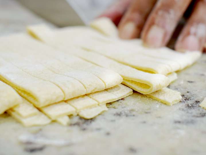 chef's hand cutting fresh pasta with a knife Shot