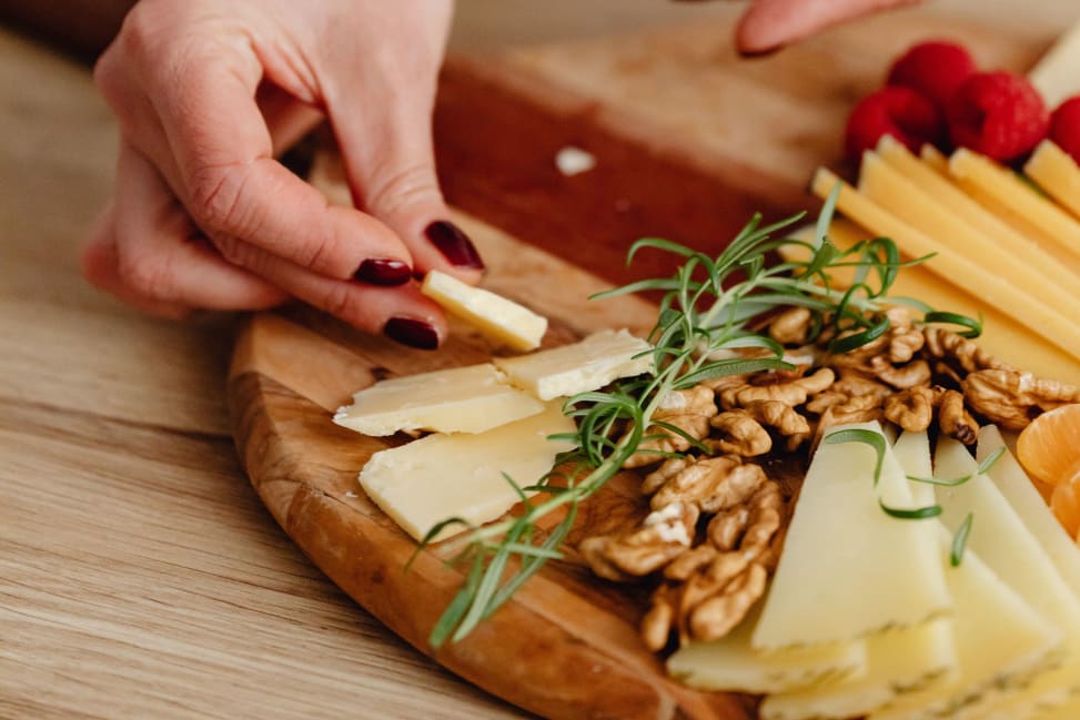 Bay Area - Hands styling a charcuterie board with sliced cheese, walnuts and fresh herbs on a wooden board Shot 2