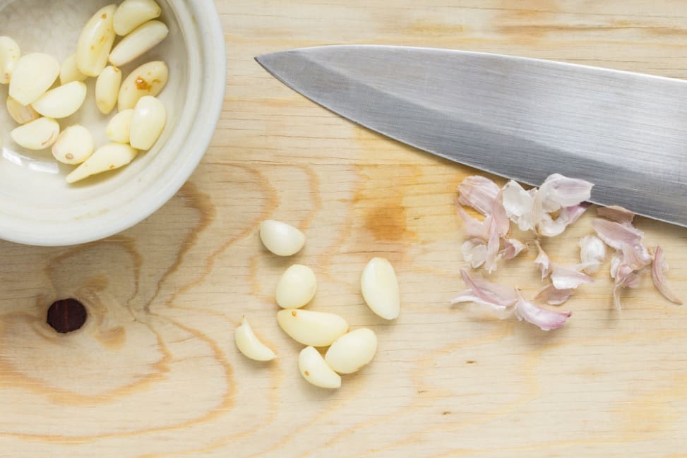 peeled cloves of garlic and a knife on a cutting board Shot 1