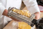 chef rolling fresh pasta dough through a pasta roller attachment Shot