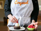 Cooking Class - Chocolate Treat Recipes in Downtown Dallas: a cooking class participant with Cozymeal apron on is decorating Flourless Chocolate Torte with Whipped Cream
