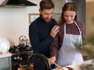 Cooking Class - Iconic New York Steakhouse - Date Night in Northern Virginia: Couple cooking together at the stove, woman chopping herbs while man stands close.