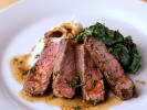 Cooking Class - Iconic New York Steakhouse - Date Night in Northern Virginia: Sliced steak with gorgonzola-shallot butter, served with creamed kale on a white plate.
