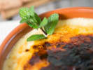 Cooking Class - One Night in Madrid in Downtown Dallas: Creamy Spanish-style custard dessert in a clay dish, topped with caramelized sugar and garnished with fresh mint leaves.