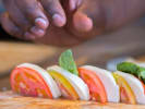Cooking Class - Savoring Italian Culinary Traditions: A chef's hand garnishing a caprese salad with basil leaves, highlighting fresh slices of tomato, mozzarella, and basil