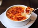 Cooking Class - Classic Parisian Bistro: A dish of creme brulee and someone taking a scoop of custard from the ramiken
