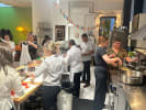 Team Building Cooking Class - Classic Puerto Rican Cooking in Manhattan: A lively cooking class scene with participants preparing food at various stations. A chef in white guides attendees