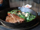 Cooking Class - Classy Steakhouse Dinner - Date Night in Northern Suburbs: A steak sizzling in a pan with sautéed vegetables and fresh herbs