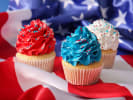 Cooking Class - Firework Cupcakes - Family Fun in Northern Virginia: Red, white, and blue cupcakes on American flag â€“ Three cupcakes with vibrant red, blue, and white frosting sitting on a crumpled American flag backdrop.