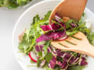 Cooking Class - Cozy Italian Supper - Date Night in Denver: Arugula and radicchio salad being tossed in a white bowl with wooden salad servers