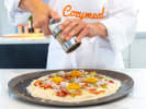 Cooking Class - Sweet and Savory Pizza Perfection in Manhattan: chef in Cozymeal apron adding toppings to carbonara-style pizza