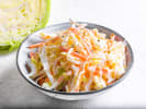 Cooking Class - British Pub Favorites in Downtown Dallas: Bowl of coleslaw with lemon and iced drink in background – A bowl of creamy shredded coleslaw placed on a light surface, with a lemon slice and iced beverage nearby.