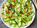 Cooking Class - Koreatown Kitchen: Tools and Techniques in Northern Suburbs: Spicy cucumber salad with red pepper and sesame – A vibrant cucumber salad garnished with red chili slices and sesame seeds, served on a white plate with chopsticks.