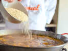 Cooking Class - Spanish Paella From Scratch: Golden saffron infused broth being poured into a paella pan of Bomba rice