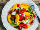 Cooking Class - Flame-Grilled Flavor in Northern Suburbs: Peach and feta salad with greens and pecans – A summer salad with sliced peaches, feta, leafy greens, roasted red peppers, and pecans on a white plate.