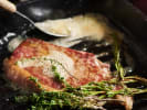 Team Building Cooking Class - Mystery Menu Challenge in Chicago: Steak searing in a pan with fresh herbs