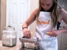 Kids' Cooking Class - Playful Pasta Learning: a young girl is wearing Cozymeal and rolling pasta dough