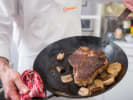 Cook & Mingle - Flavorful Gatherings: chef in a Cozymeal apron presenting a freshly cooked steak in a pan
