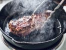 Cooking Class - Iconic American Steakhouse: chef searing a steak in a cast iron pan
