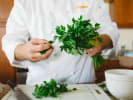 Cooking Class - Ribeyes to Galettes - Date Night in Downtown Dallas: Chef holding fresh parsley in kitchen – A chef in a white coat holding a bunch of fresh parsley, mid-prep in a bright kitchen.
