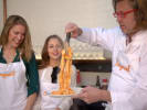 Cooking Class - Make Fresh Pasta & Bolognese in Downtown Dallas: group of cooking class participant with Cozymeal aprons on are making tomato sauce coated pasta