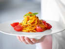 Cooking Class - Linguine With a Kick in Houston: a person holding an elegantly served linguine pasta plate with tomatoes on the sides