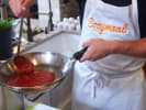 Cooking Class - Linguine With a Kick in Houston: a person with Cozymeal apron on is making tomato based sauce in a pan