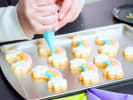 Cooking Class - Decorating Cookies With Royal Icing: person decorating rainbow cookies with royal icing