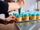 Cooking Class - Firework Cupcakes - Family Fun in Northern Virginia: Piping blue frosting onto cupcakes â€“ Close-up of hands squeezing blue frosting onto yellow cupcakes on a baking tray.