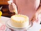 Cooking Class - Master Elegant Cake Decorating in Northern Suburbs: piping buttercream ornaments on vanila sponge cake next to a batch of edible pink sugar flowers for decoration later on