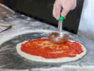 Online Team Building Cooking Class - Homemade Pizza: putting tomato sauce on pizza